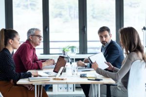 A group of architects meeting with the team from Overhead Door Company of Huntsville to discuss new garage doors to be installed. There are two men and two women seated around an rectangular table with bright light streaming in from the windows.