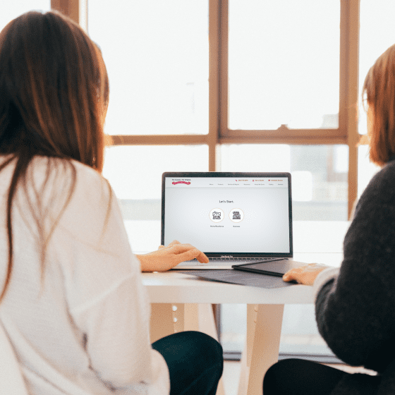 A customer sitting at work looking at the schedule an appointment with Overhead Door tool found on the company website. Two ladies sitting with their backs turned to the camera. They are scheduling an appointment to view Overhead Garage Door Products.