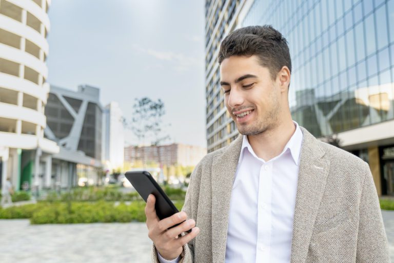 Young cheerful businessman in formalwear looking at screen of mobile phone