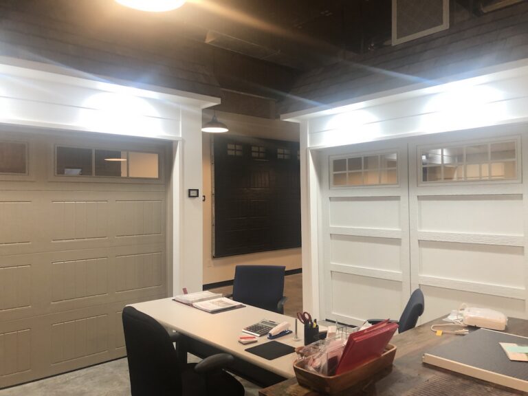 The showroom of Overhead Door Company of Huntsville/North Alabama located at 9550 Madison Alabama serving North Alabama. the picture shows three garage doors and there are more with fully operational doors. One is white and from the courtyard series, one is taupe from the thermacore line and the other is brown from the traditional steel line along with samples and openers.