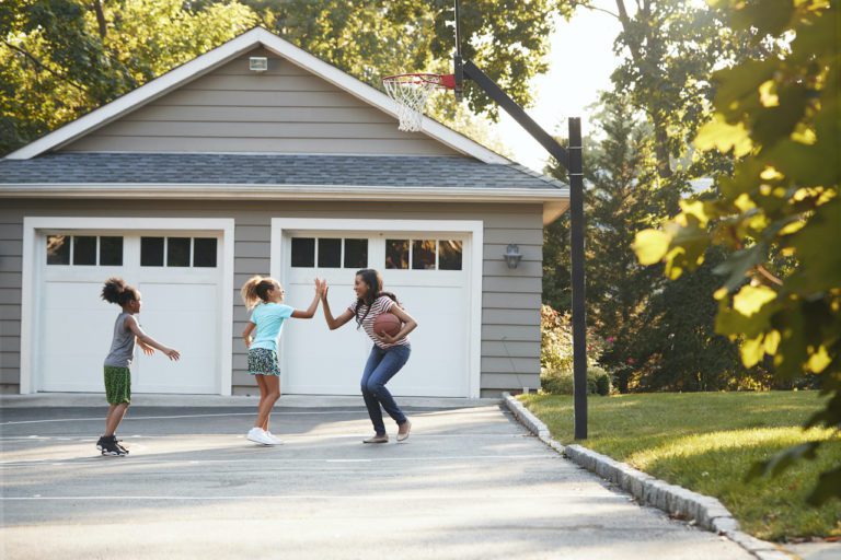 A mother playing basketball with her two daughters in a driveway located in front of her new courtyard style garage doors from Overhead Door Company in Huntsville/North Alabama. The garage door is in good working order because it has had regular maintenance upkeep on their doors.