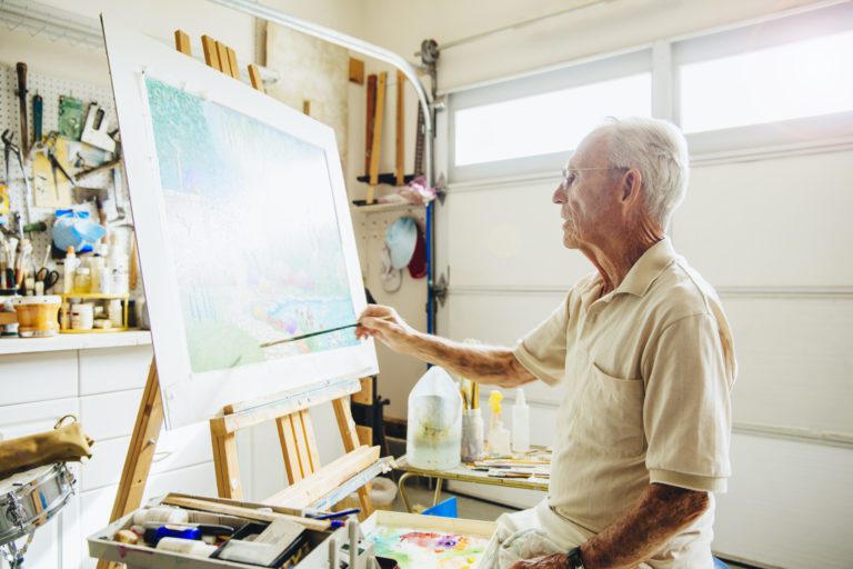 Old Man painting in front of his new Garage Door from Overhead Door Company of Huntsville™. He's made a space for his hobbies inside his garage. The garage door allows plenty of light to stream in through its windows.