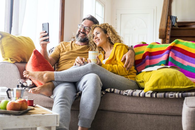 A happy caucasian couple sitting on a cheerful couch talking to an Overhead Door Company representative about scheduling the installation of their new garage door.