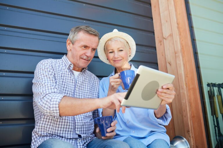 Overhead Door Company offers many garage doors services as shown on their website. A couple in their sixties sitting by a closed garage door looking at a laptop completing the contact form found on the Overhead Door Company of Huntsville website. They are smiling because of the easy convenience of this form to schedule their garage door service.