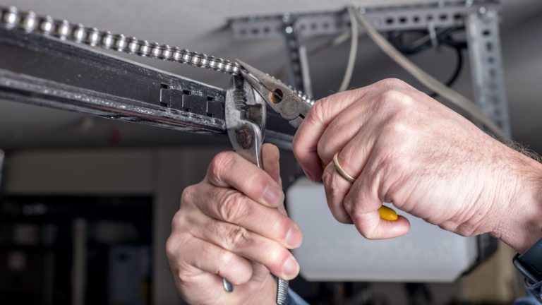 Man working on a garage door opener the chain. Picture shows two hands with pliers.