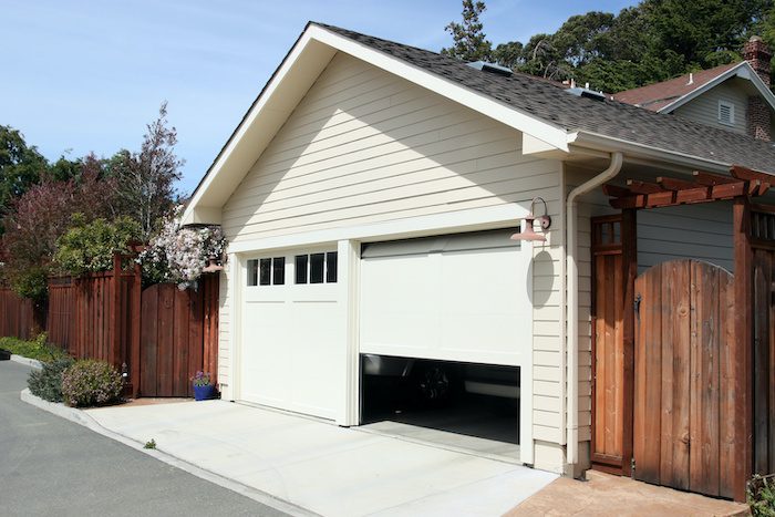 A beautiful white garage door that is cracked to let cooler air inside. The garage door is broken and won't open due to a broken spring.