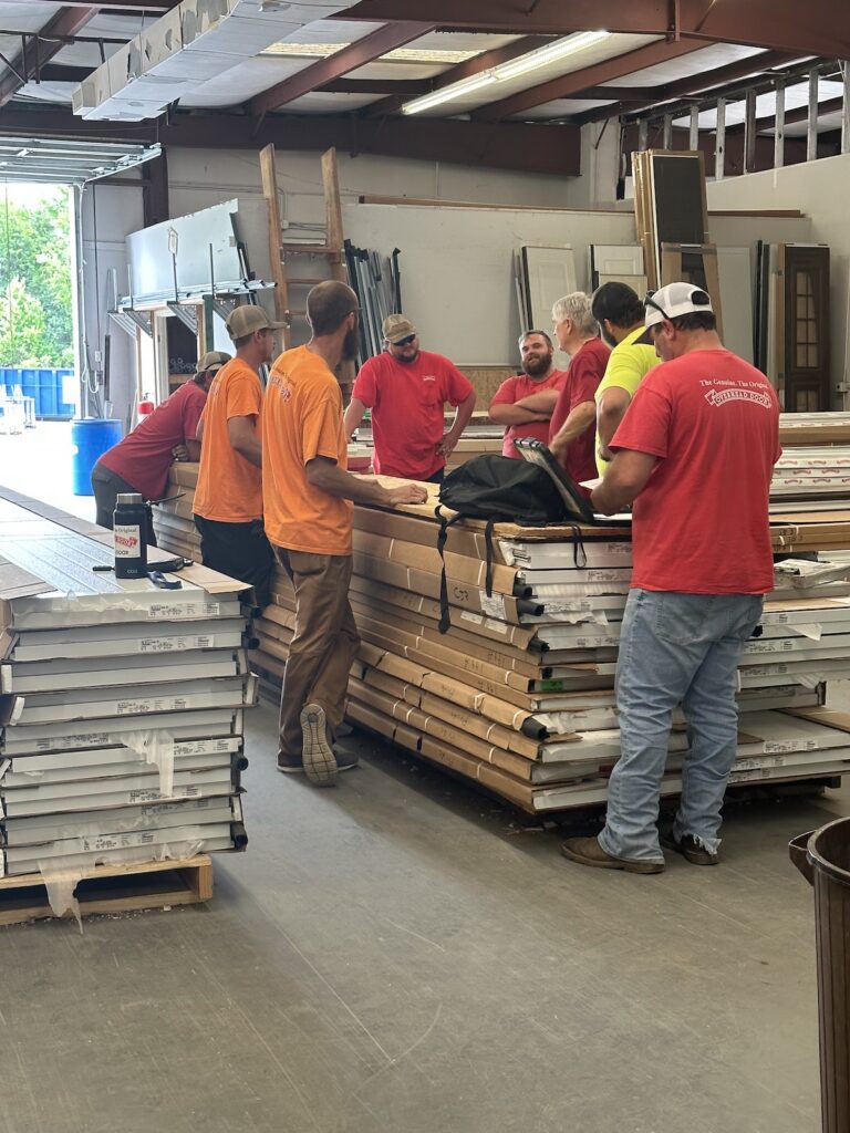 Garage Door Techs from Overhead Door Company of Huntsville/North Alabama standing around a stack of garage door panels to be installed in Meridianville and Madison, Alabama. They are discussing the schedule for the day.