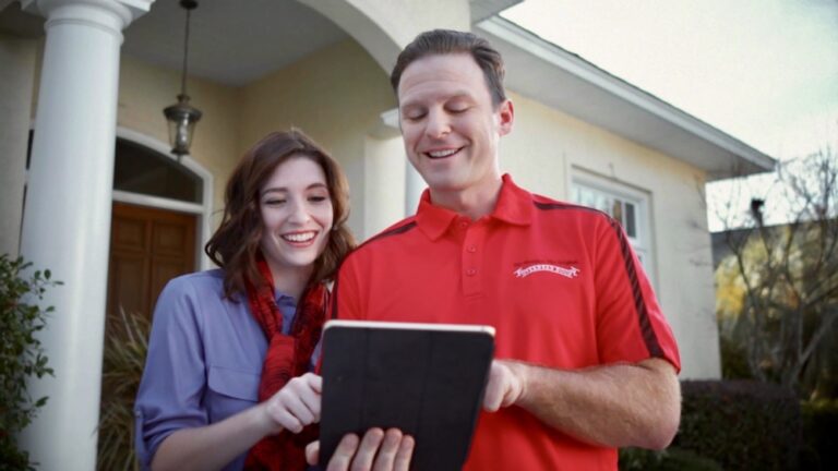 Garage Door service employees for Overhead Door Company looking at iPad and describing the company and its history. The man is wearing a shirt with the words Overhead Door Company on it. The woman is wearing a blue shirt. They are sharing one iPad.